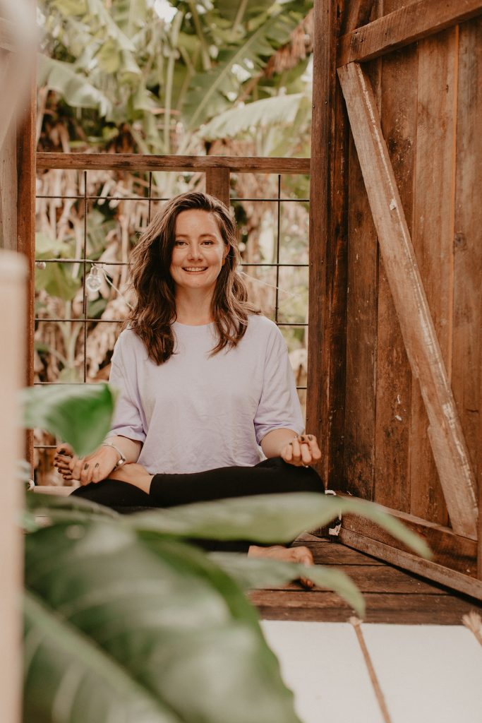 A woman sits in a meditation position, smiling